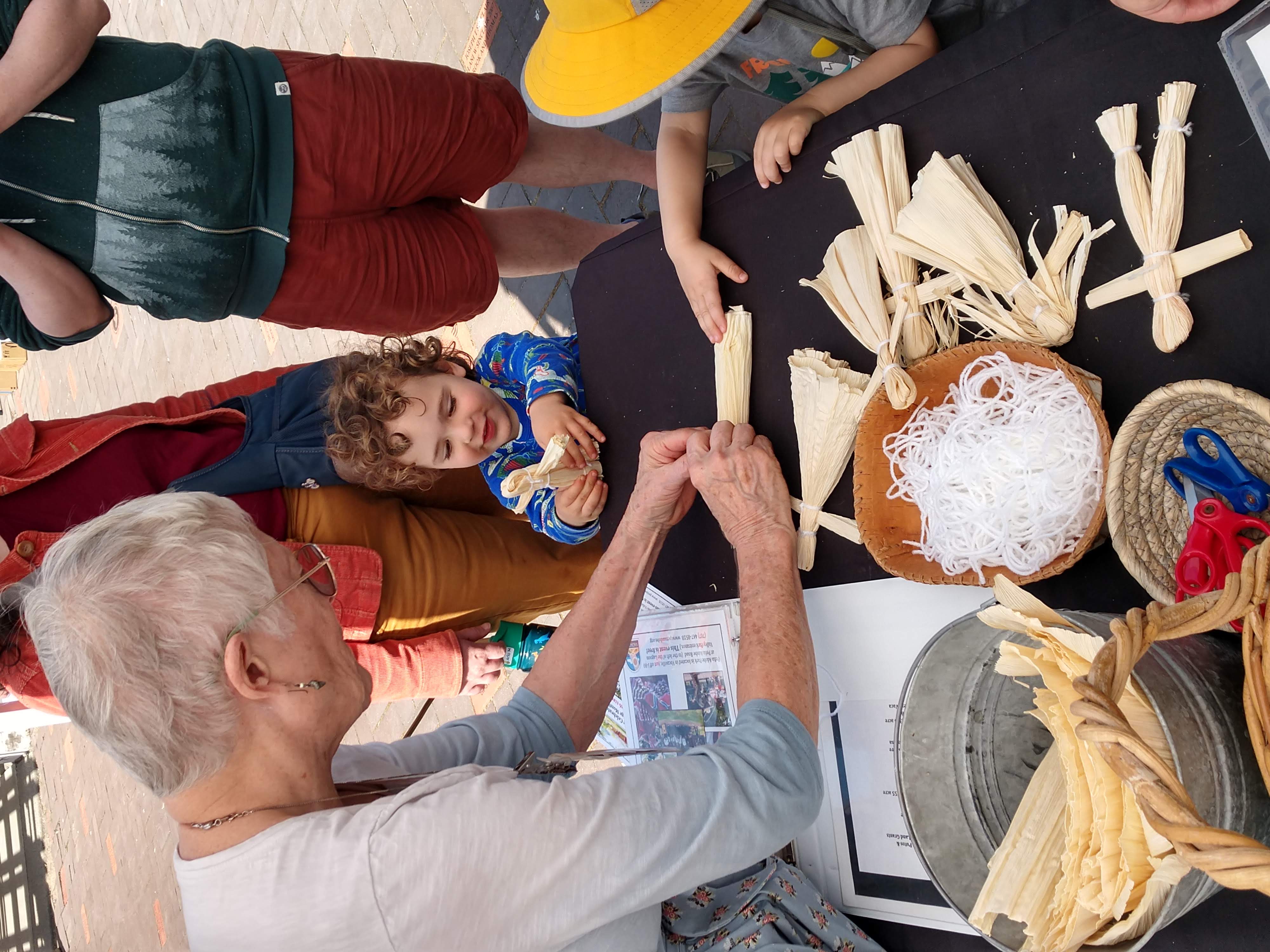Peña Adobe Historical Society Docent Melody Johnston helps Rush Ranch park visitor make a corn husk doll!