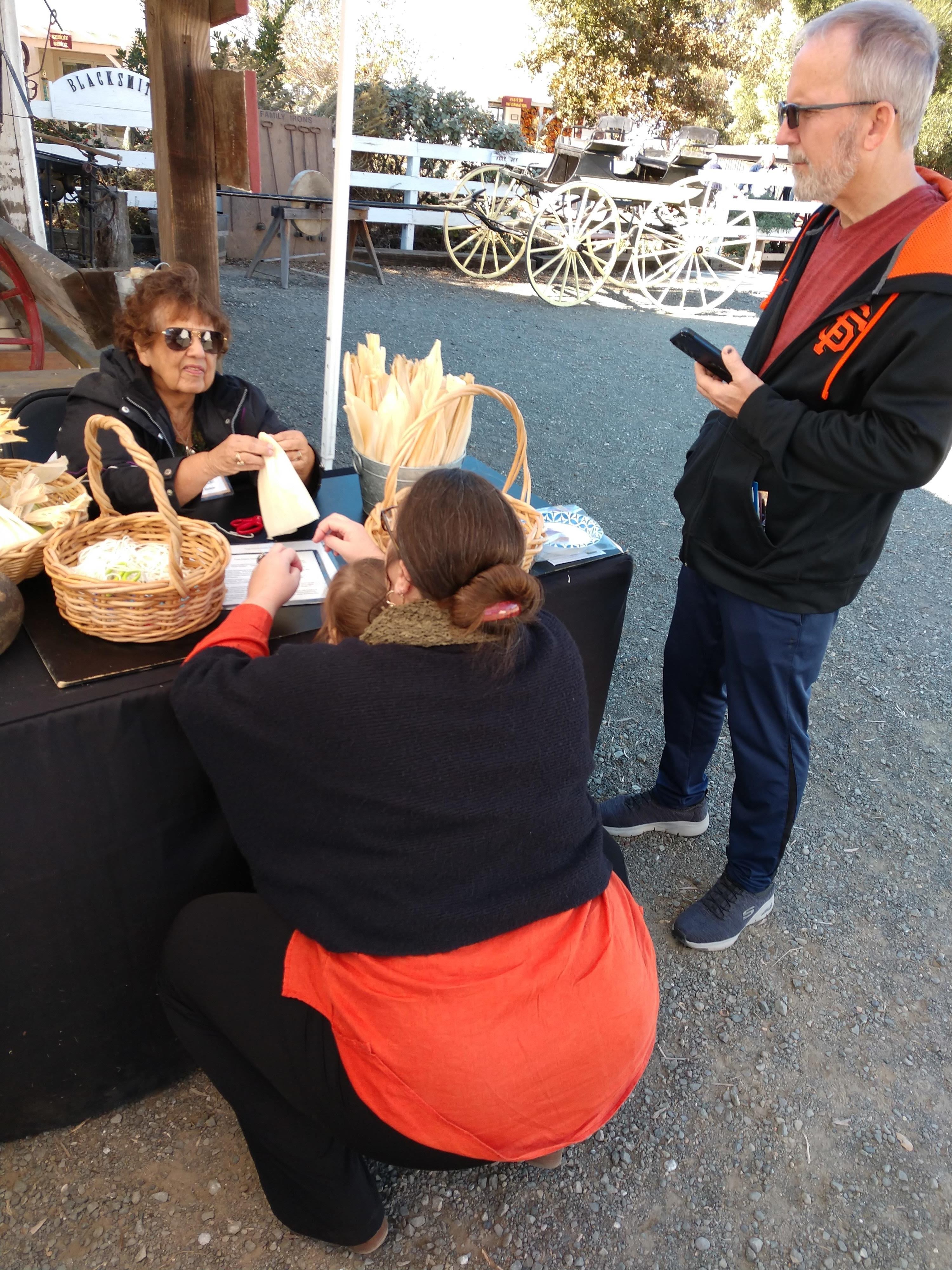 Peña Adobe Historical Society volunteer Darlene helps a young visitor and her Mom make a corn husk doll at Rush Ranch's Harvest Festival.